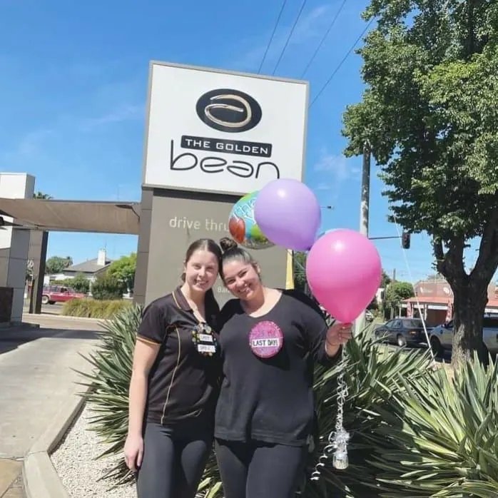 Two Golden Bean team members with balloons outside the store
