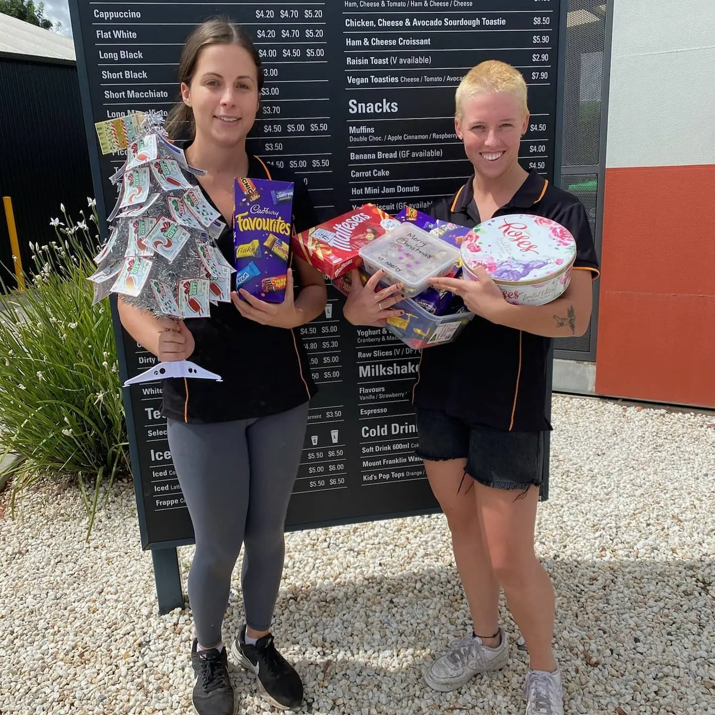 Two Golden Bean team members holding gifts in front of the menu board